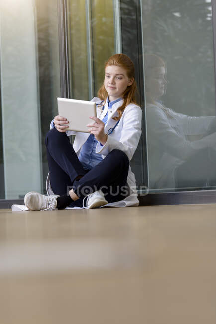 Doctora joven mirando tableta digital en la entrada del hospital - foto de stock