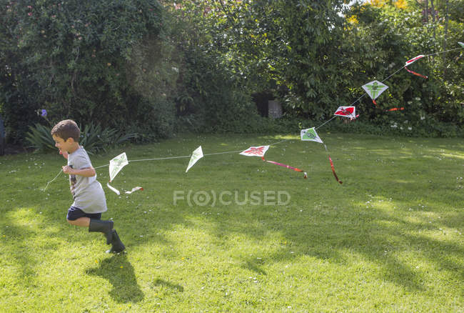 Menino correndo no jardim segurando pipa — Fotografia de Stock