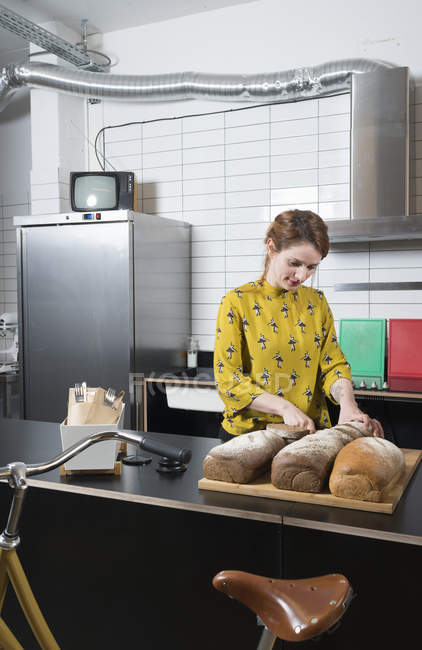 Waitress slicing bread at counter of hipster bike repair cafe — Stock Photo