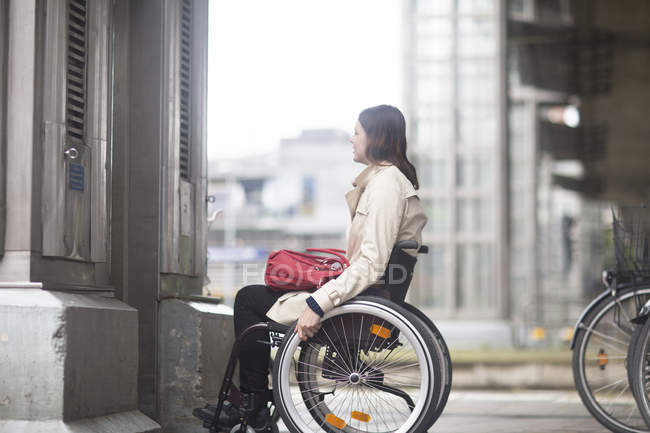 Mujer joven en silla de ruedas esperando el ascensor de la ciudad - foto de stock