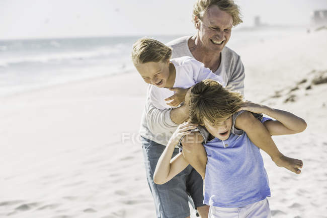 Vater hilft Söhnen huckepack am Strand — Stockfoto