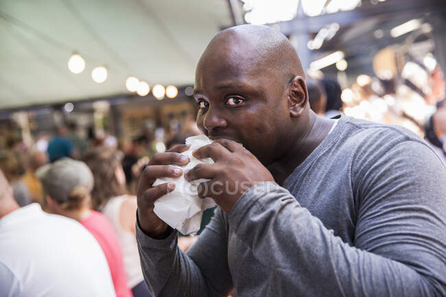 Male customer eating burger at cooperative food market stall — Stock Photo
