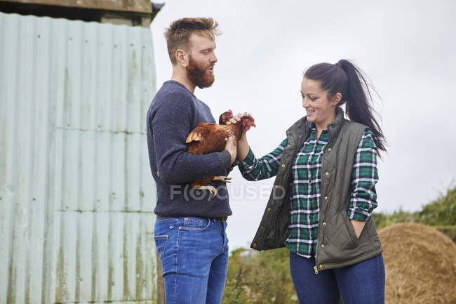 Casal jovem na fazenda de frango segurando galinhas — Fotografia de Stock