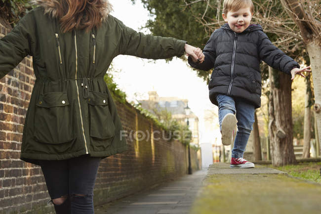 Женщина, держащая малыша за руку, идет по стене улицы — стоковое фото