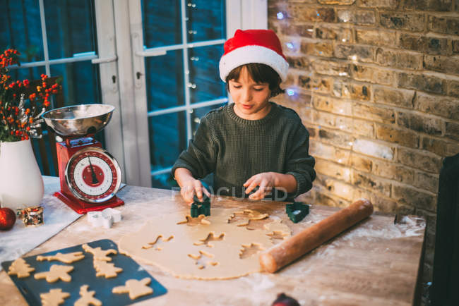 Ragazzo in cappello Santa preparazione biscotti di Natale al bancone della cucina — Foto stock