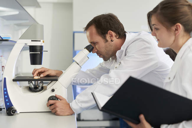 Científico en laboratorio mirando a través del microscopio - foto de stock