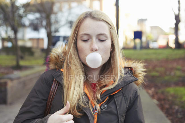 Portrait of young woman, outdoors, blowing bubble with bubblegum — Stock Photo