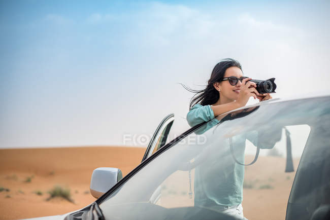 Turista femenina fotografiando desde vehículo todoterreno en el desierto, Dubai, Emiratos Árabes Unidos - foto de stock