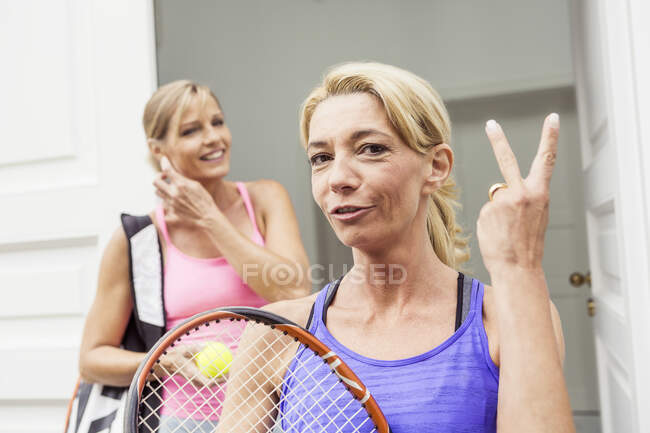 Portrait of two mature female tennis players, one making two finger gesture — Stock Photo
