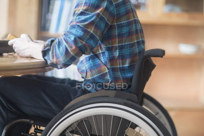 Jeune homme utilisant le panneau de commande de connexion en fauteuil roulant et transformateur à la table de cuisine — Photo de stock