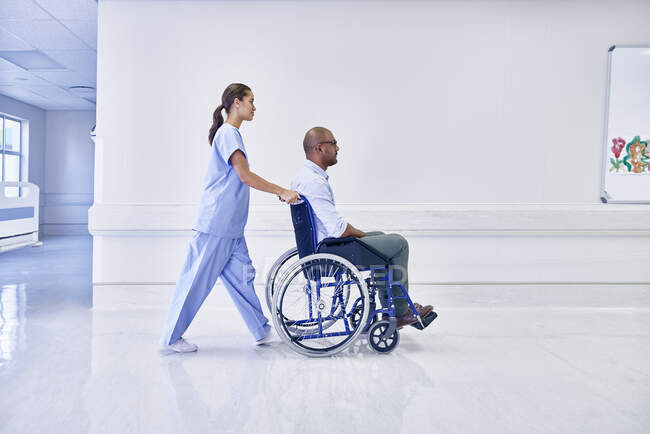 Médico en hospital empujando paciente en silla de ruedas - foto de stock