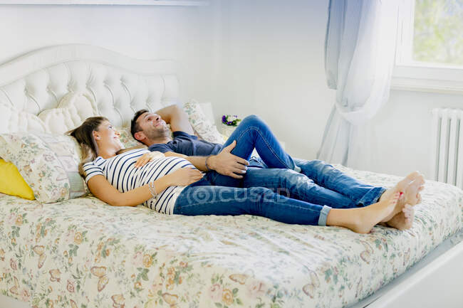 Casal grávida deitado na cama sorrindo — Fotografia de Stock