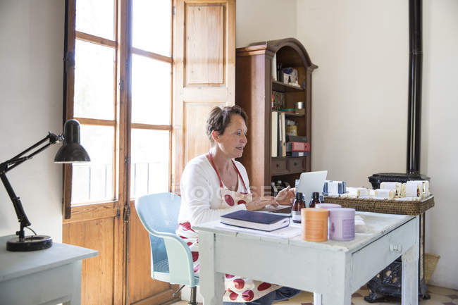 Mulher madura digitando no laptop do escritório na oficina de sabão artesanal — Fotografia de Stock
