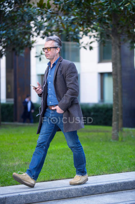 Man with smartphone and earbuds walking outdoors — Stock Photo