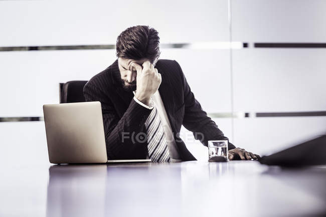 Hombre de negocios estresado con la mano en la frente en el escritorio de la oficina - foto de stock