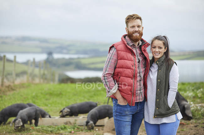 Casal na fazenda de suínos olhando para a câmera sorrindo — Fotografia de Stock