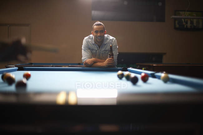Man with beer leaning against pool table, smiling — Stock Photo