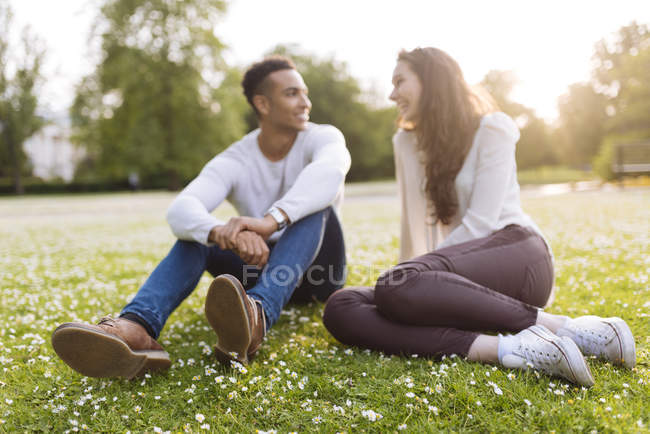 Молодая пара сидит на траве лицом к лицу улыбаясь — стоковое фото
