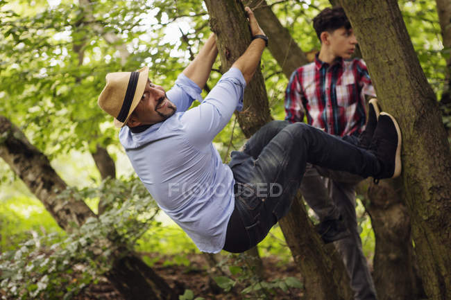 Portrait of father and son, fooling around, hanging in tree — Stock Photo