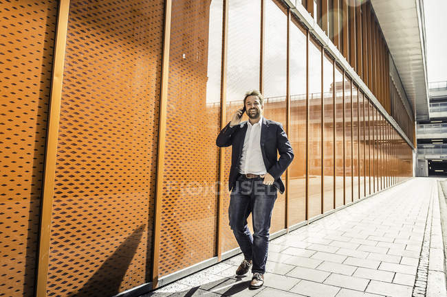 Geschäftsmann telefoniert mit Smartphone, während er vor Bürogebäude spaziert — Stockfoto