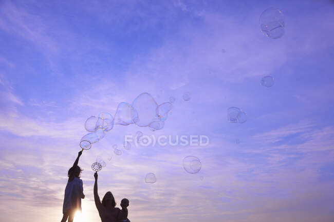 Silhouetted woman with baby son and daughter blowing bubbles against blue sky, Buonconvento, Tuscany, Italy — Stock Photo