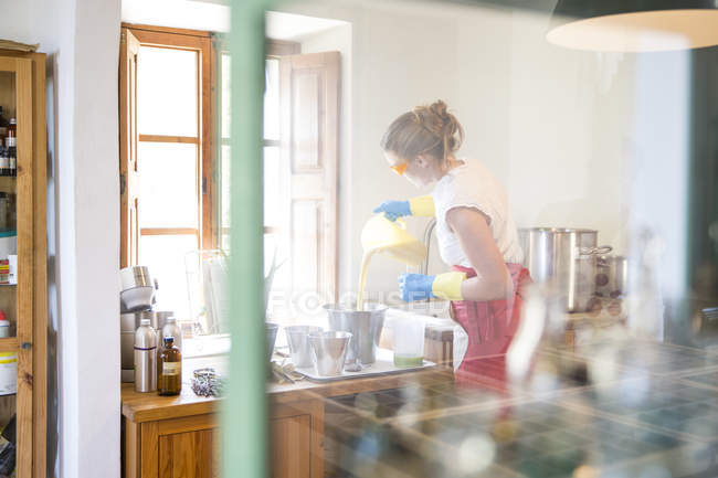 Молодая женщина наливает жидкое лавандовое мыло в миску в мыльной мастерской ручной работы — стоковое фото