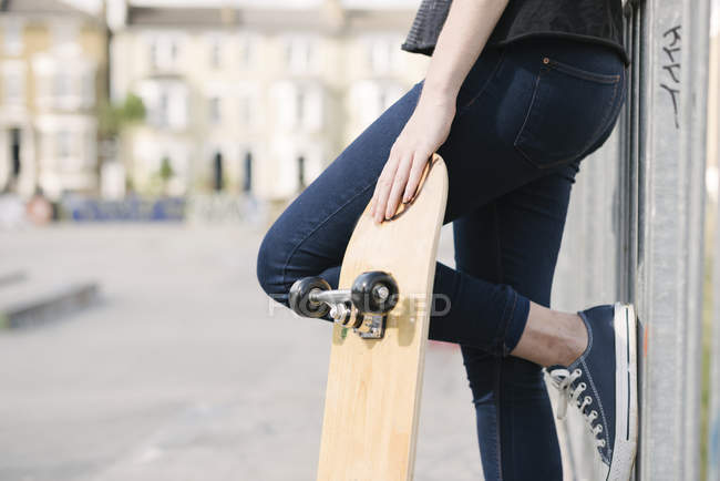Талія вниз жіночого скейтбордера, що спирається на паркан в скейтпарку — стокове фото
