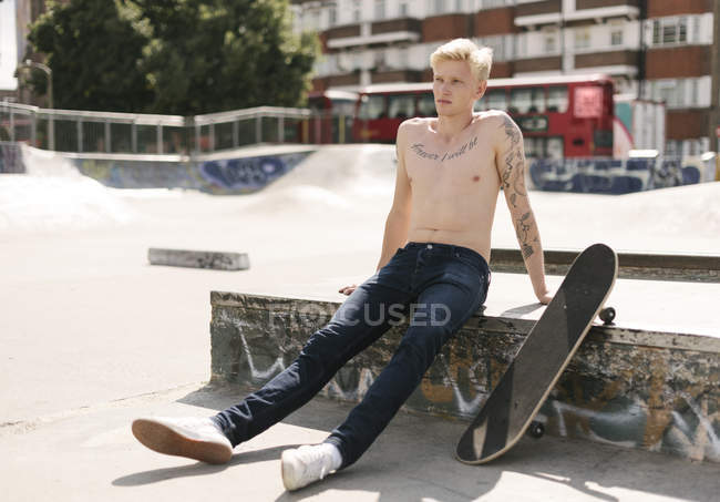 Tätowierter junger männlicher Skateboarder sitzt im Skatepark — Stockfoto