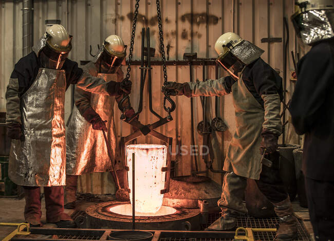 Male foundry workers winching white hot melting pot in bronze foundry — Stock Photo