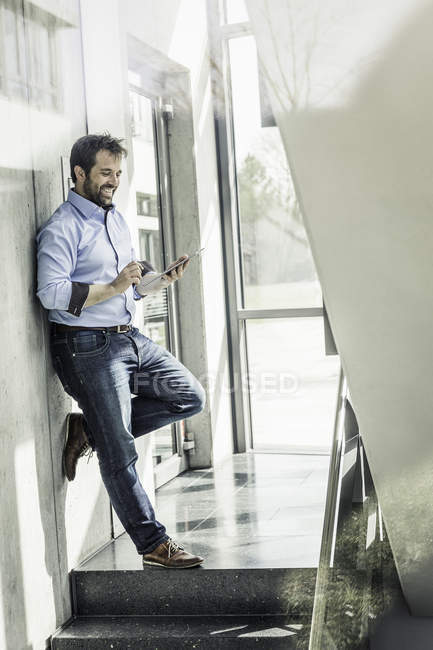 Geschäftsmann lehnt mit digitalem Tablet-Touchscreen an Bürowand — Stockfoto