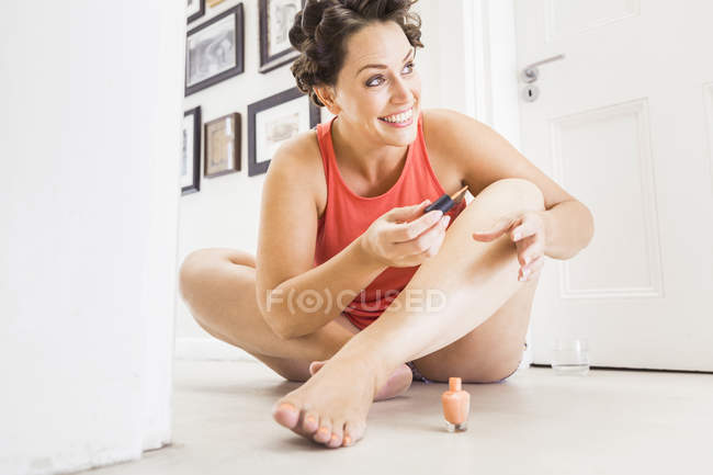 Mujer con rodillos de espuma en el pelo, pintando uñas de los pies - foto de stock