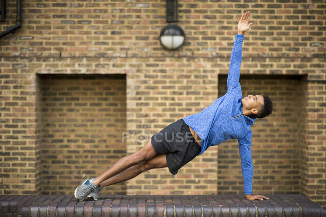 Hombre estirándose frente a la pared de ladrillo, Wapping, Londres, Reino Unido - foto de stock