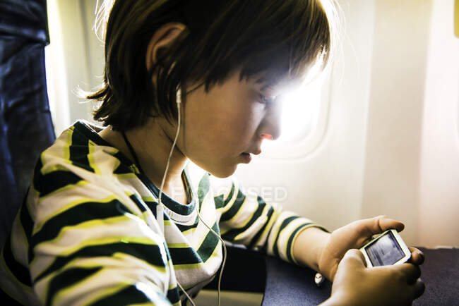 Мальчик на самолете выбирает музыку на mp3 плеере — стоковое фото