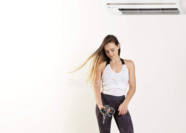 Mulher segurando pular corda sob ar condicionado, fundo branco — Fotografia de Stock