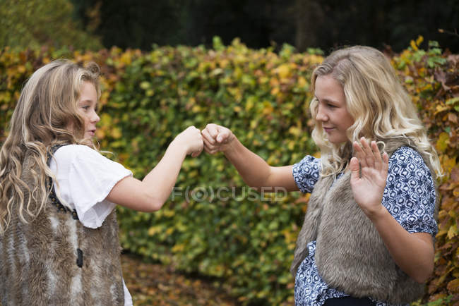 Duas irmãs fazendo solavancos de punho por sebe de jardim — Fotografia de Stock