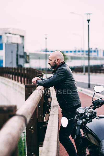 Mature male motorcyclist looking out from roadside railing — Stock Photo