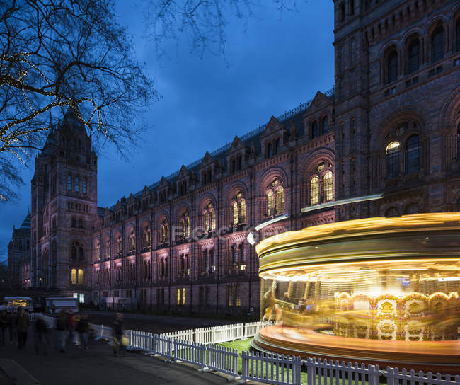 Carrousel de filage éclairé par le Musée d'histoire naturelle au crépuscule, Londres, Royaume-Uni — Photo de stock
