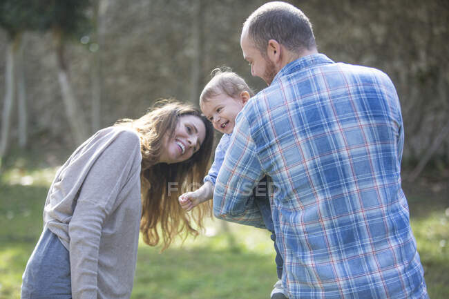 Padres sosteniendo niño sonriente, jugando - foto de stock