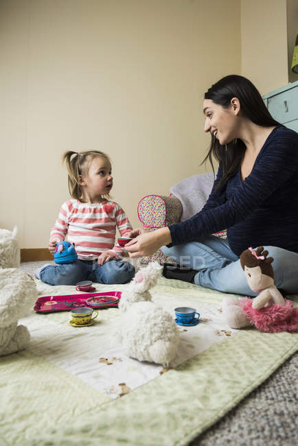Criança feminina sentada no chão com a mãe grávida jogando piqueniques com brinquedos macios — Fotografia de Stock