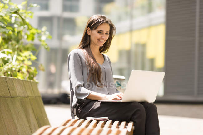 Businesswoman typing on laptop on park bench, London, UK — Stock Photo