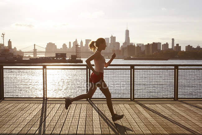 Side view of woman jogging on pier, Manhattan, New York, USA — Stock Photo
