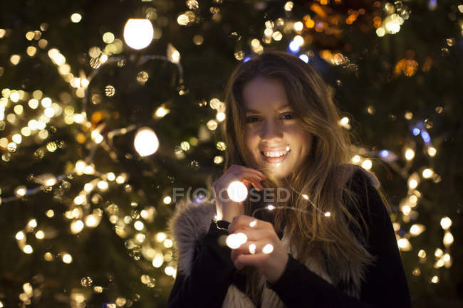 Mujer joven con luces en la mano, árbol en el fondo - foto de stock