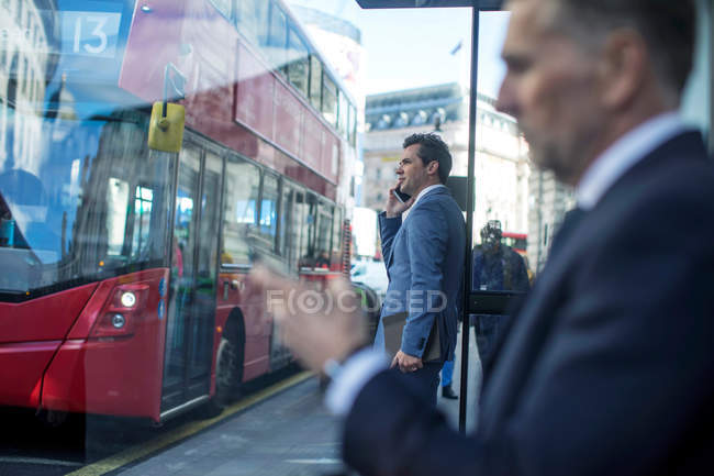 Бизнесмен, ожидающий автобуса на остановке с помощью смартфона, Лондон, Великобритания — стоковое фото