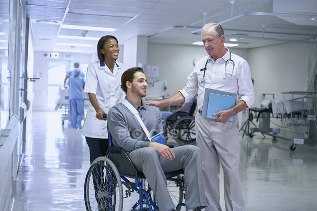 Доктор консультування з людиною в інвалідному кріслі з ручним слінгом — стокове фото