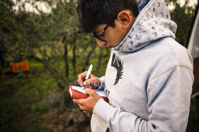 Молодой человек собирает урожай в винограднике, пишет заметки — стоковое фото