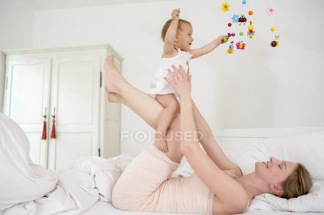 Mother lifting baby daughter on bed — Stock Photo
