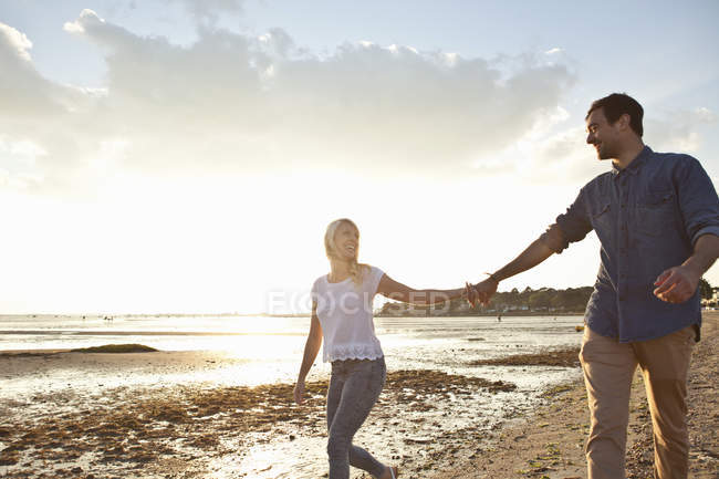 Jeune couple marchant sur une plage ensoleillée — Photo de stock