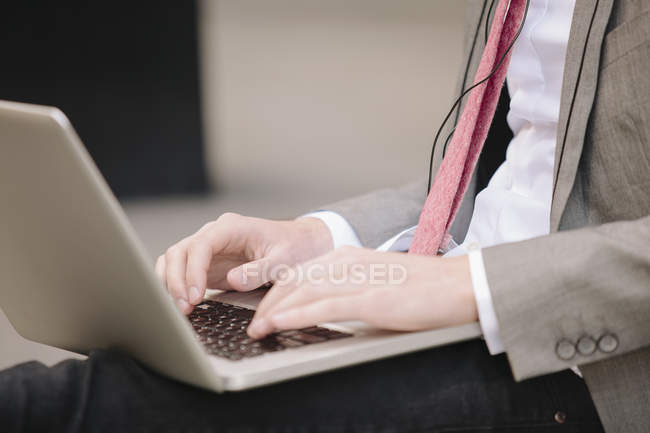 Recortado disparo de joven empresario de la ciudad sentado en la acera escribiendo en el ordenador portátil - foto de stock