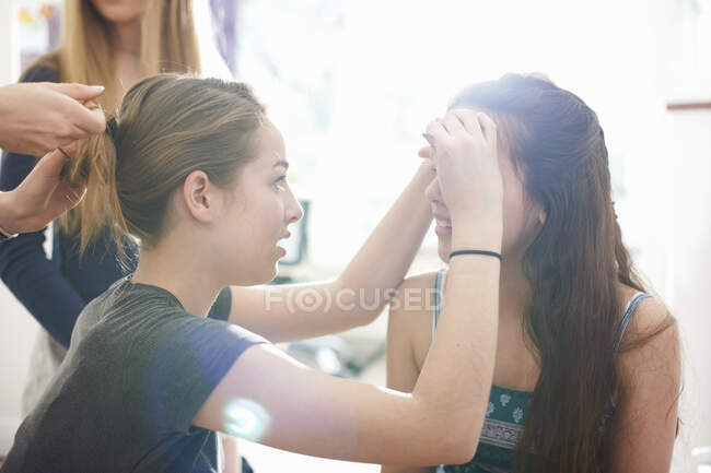 Quatro adolescentes fazendo uns aos outros cabelo e maquiagem no quarto — Fotografia de Stock