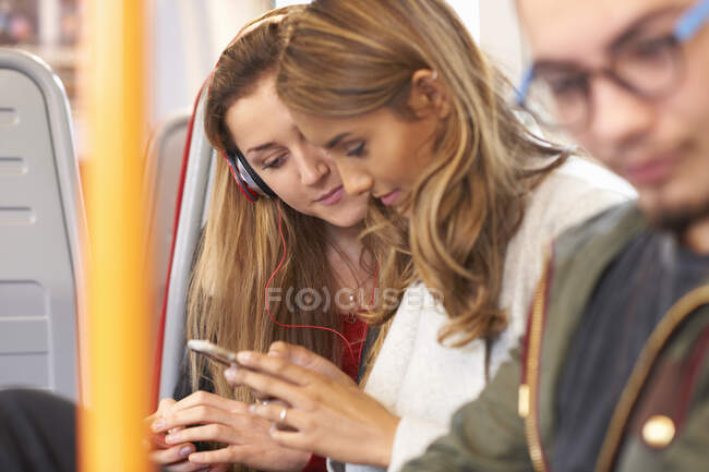 Two young female friends on train, looking at smartphone — Stock Photo